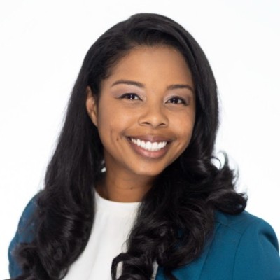 Laura Teclemariam smiles for a professional headshot against a white background, wearing a blue sweater.