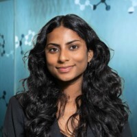 Benecia Jude smiles for her professional headshot in front of a light blue backdrop