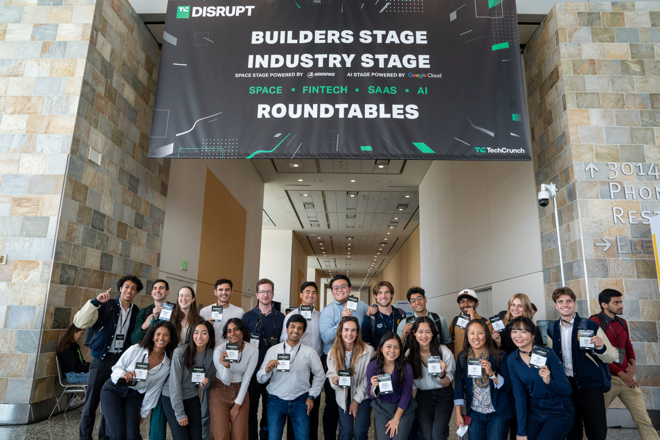 The Berkeley TechCrunch Delegation smiles for a group photo under a banner marking the entrace to the Roundtables arena at the TechCrunch conference.