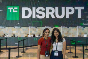 Amy Jain and Shristi Dalal pose for a photo together in the lobby of the Moscone Center in front of a large black and green TechCrunch banner.