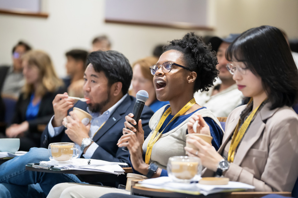 Judges Jay Onda, Stacey King, and Sandy Diao sit in the front row enjoying ice cream. Stacey speaks into a microphone.