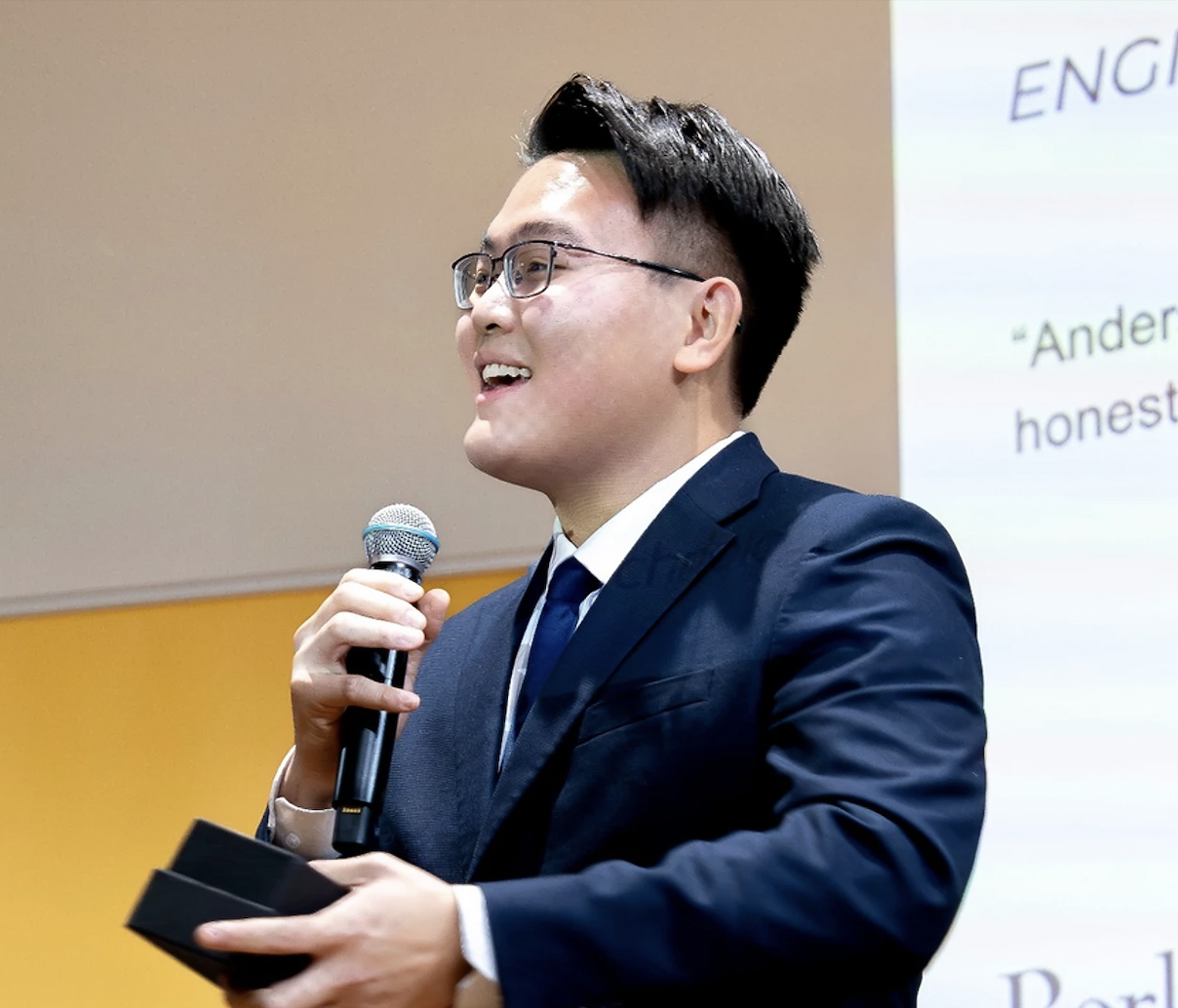 Anderson Lam speaks into a microphone. A slide projected on the background reads "ENGIN 183B" and contains positive reviews of Anderson's facilitation.