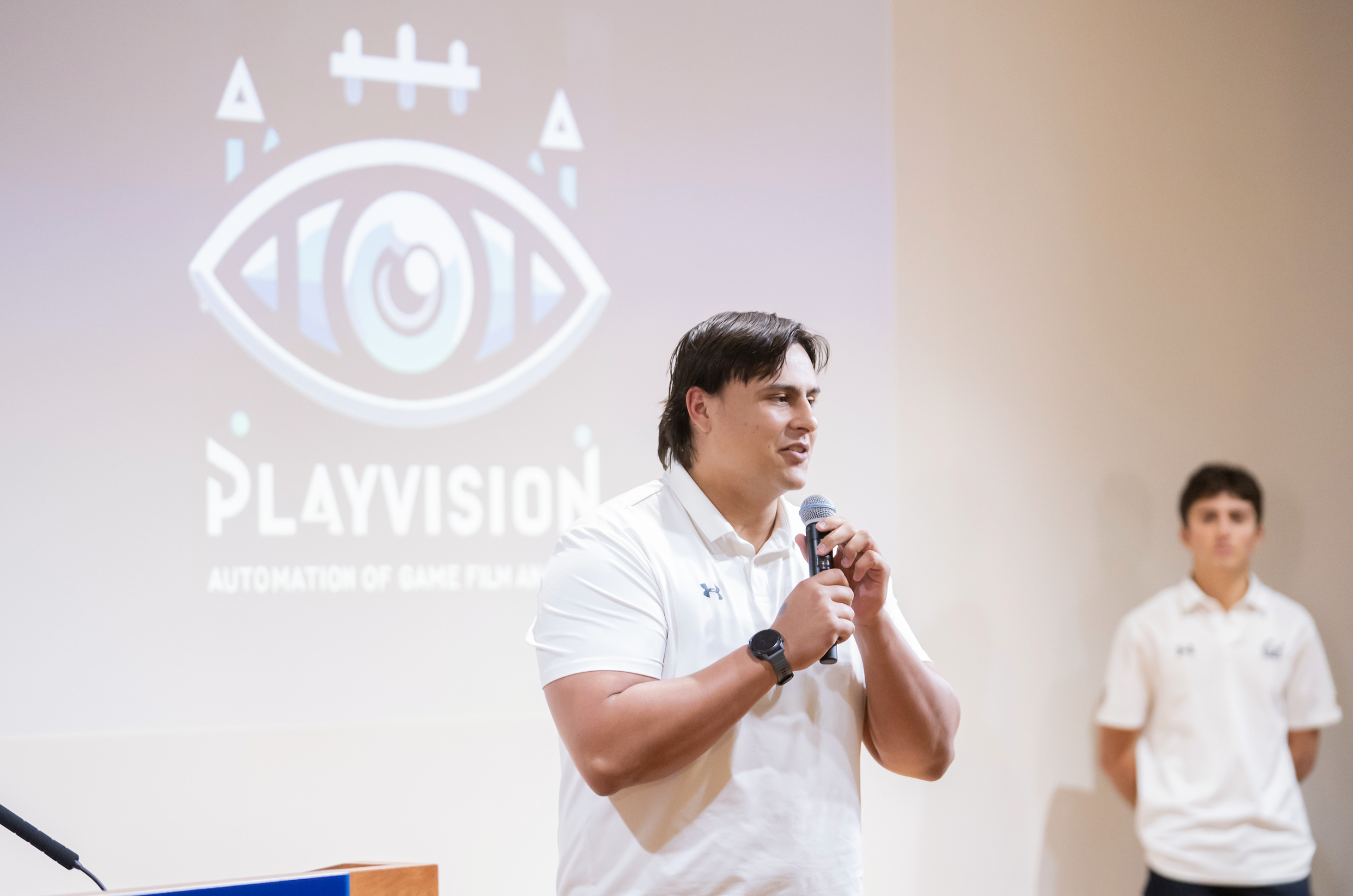 Ender Aguilar speaks at Collider Cup XIV, presenting a slide with the Playvision logo, an eye surrounded by sports equipment.