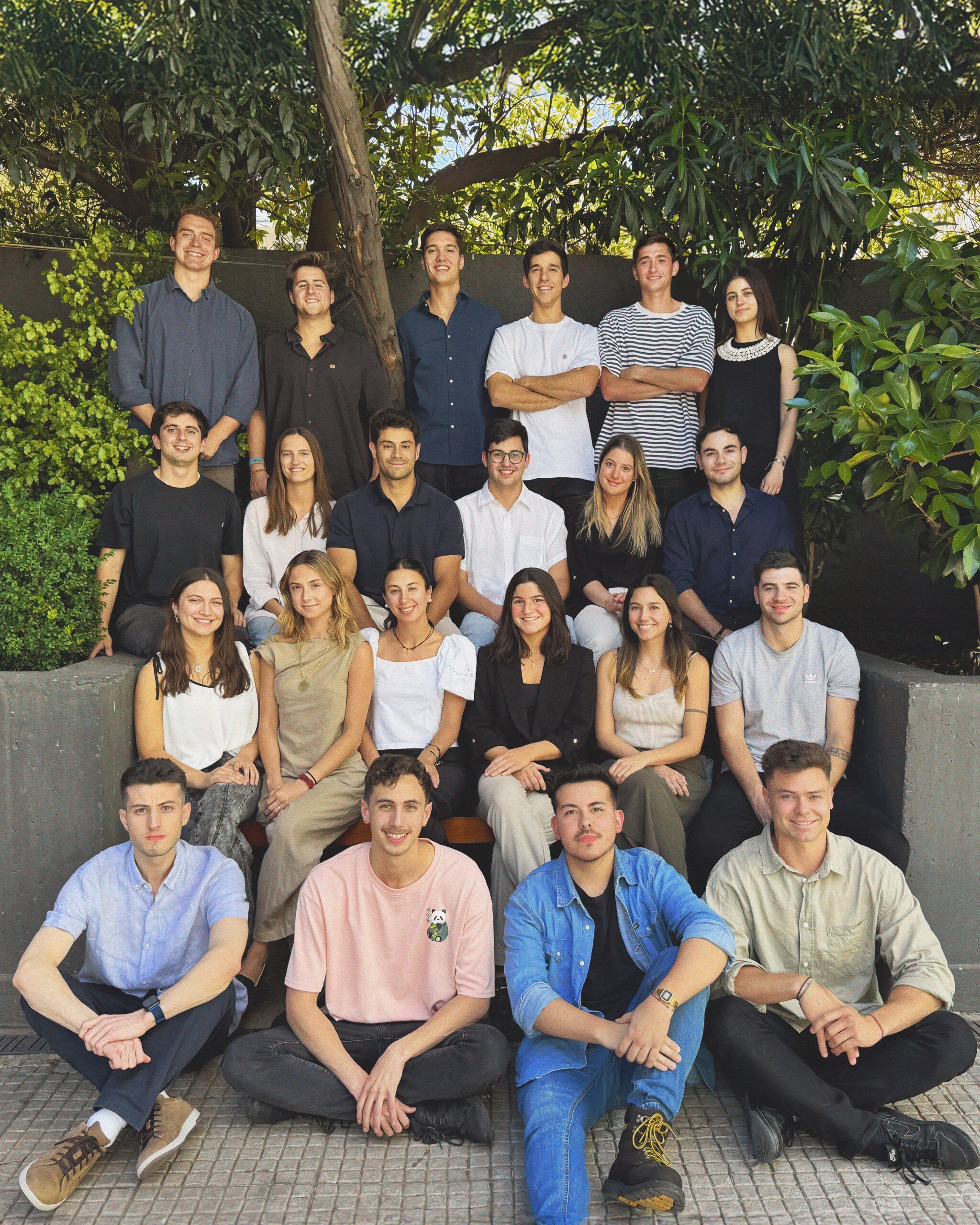 The Vambe team smiles for a company photo outside against a green backdrop in indirect shade