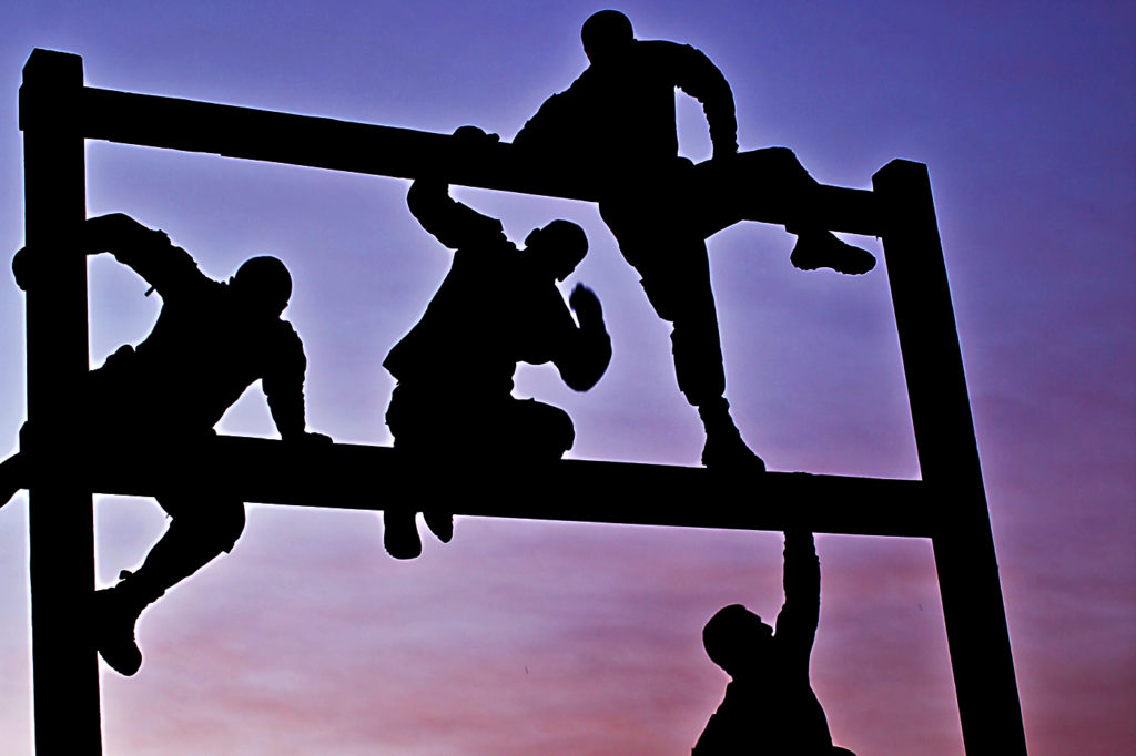 4 individuals climbing up a symbolic barrier fence